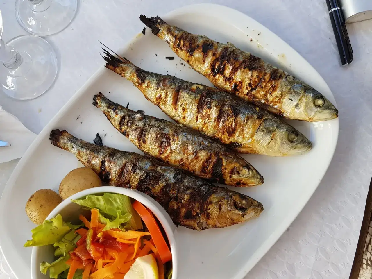 Quatre sardines grillées, dorées et savoureuses, accompagnées de pommes de terre et d'une salade fraîche. Un délice !