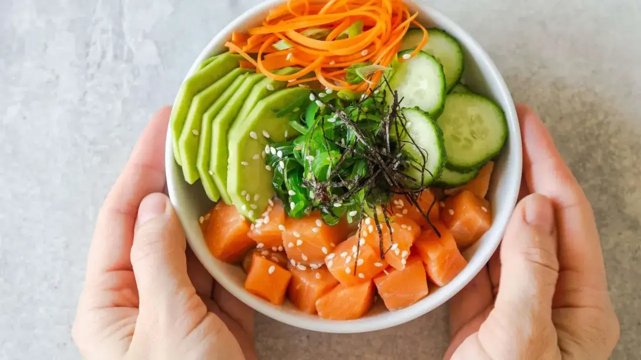Un bol coloré de saumon cru, avocat, concombre, carottes râpées et algues, parfait pour une recette souper légère et saine.