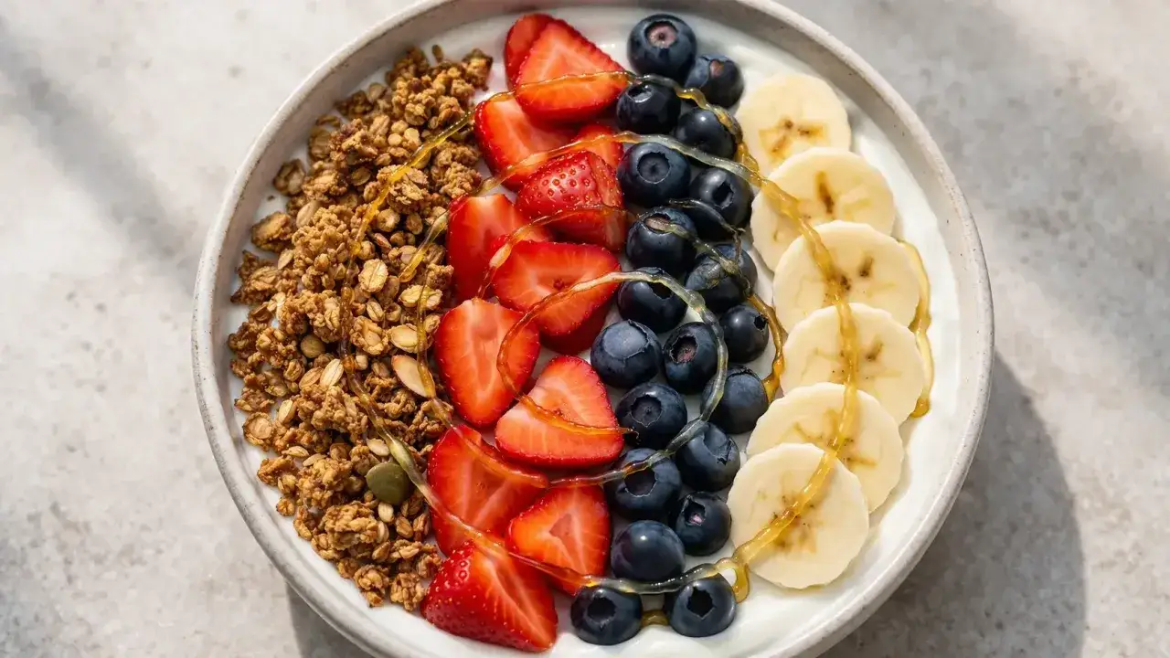 Un bol de granola, fraises, myrtilles et bananes arrosé de miel. Une recette avec fromage blanc pour un petit-déjeuner sain et gourmand.