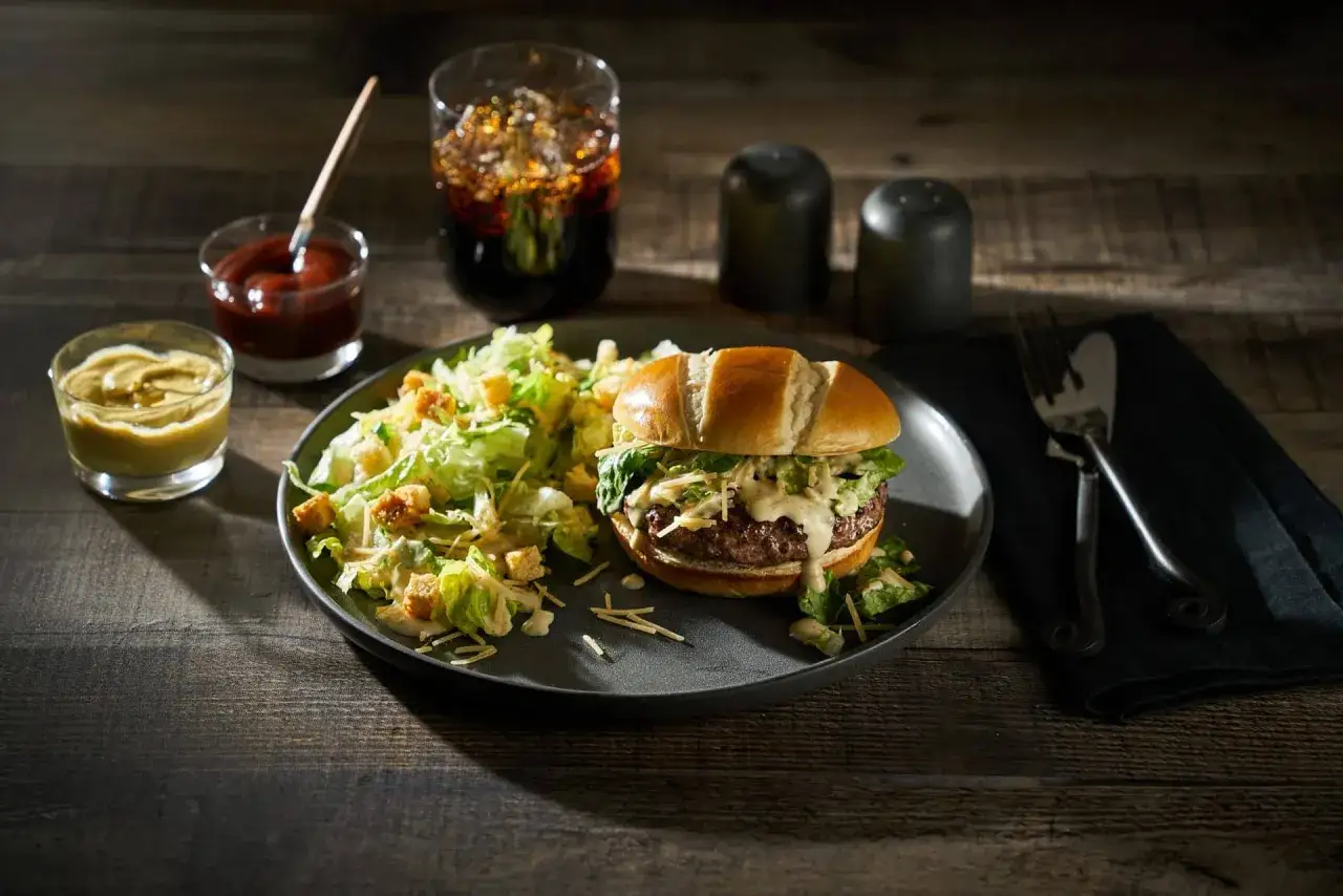 Un délicieux burger avec une salade César croustillante, servi avec des condiments et une boisson pétillante.