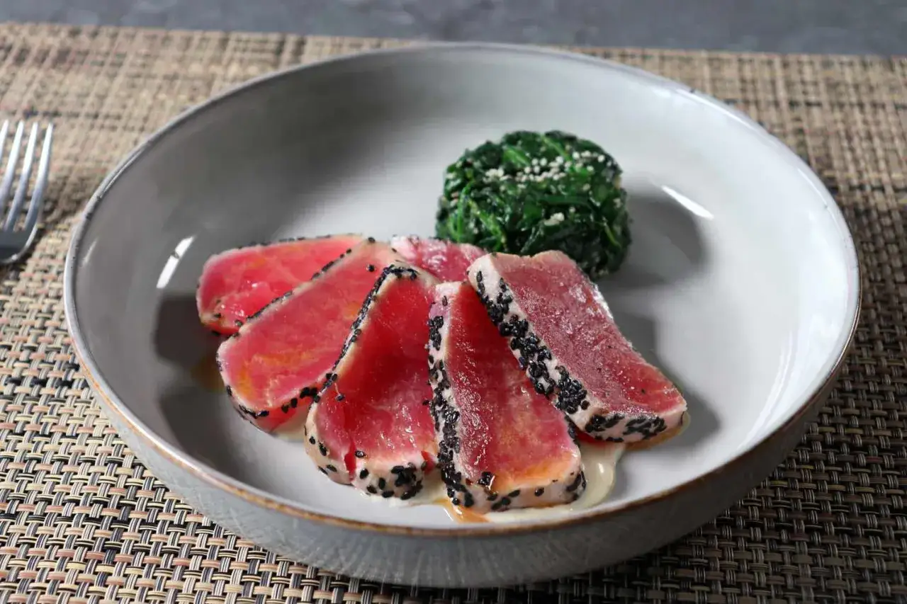 Tranches de tataki de thon poêlé, enrobées de sésame noir, servies avec une portion d'épinards.