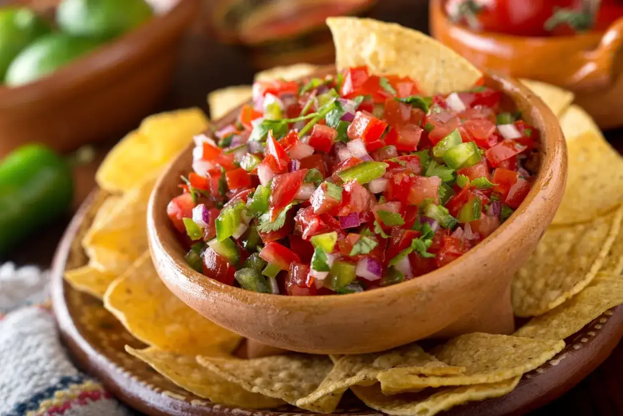 Un bol en terre cuite rempli de salsa facile, garni de coriandre fra&icirc;che, entour&eacute; de croustillantes chips de tortilla.