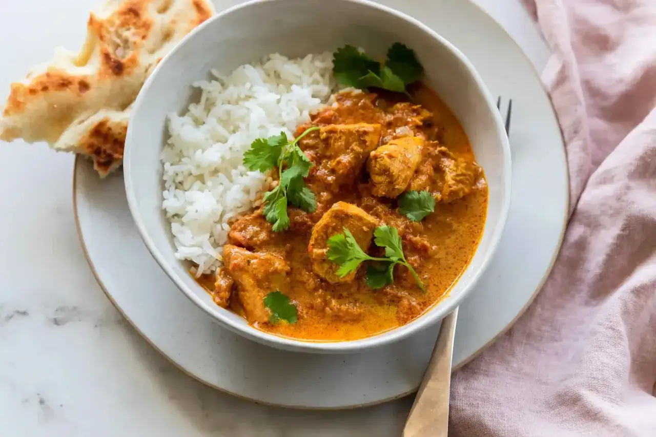 Un bol de riz blanc et de butter chicken crémeux, garni de coriandre fraîche, servi avec du pain naan.