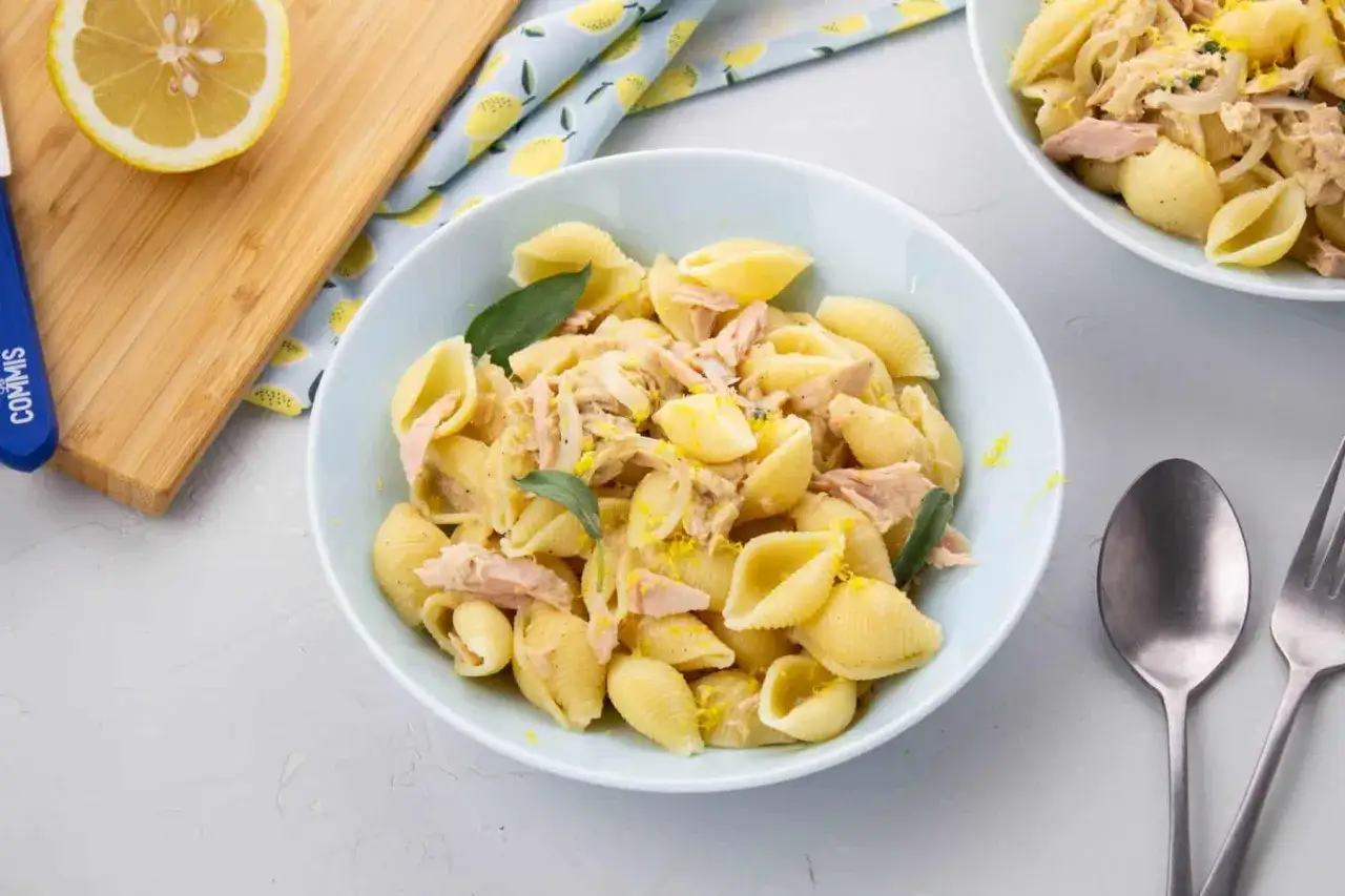 Un plat de pâtes au thon, garni de feuilles de sauge et de zeste de citron, prêt à être dégusté.