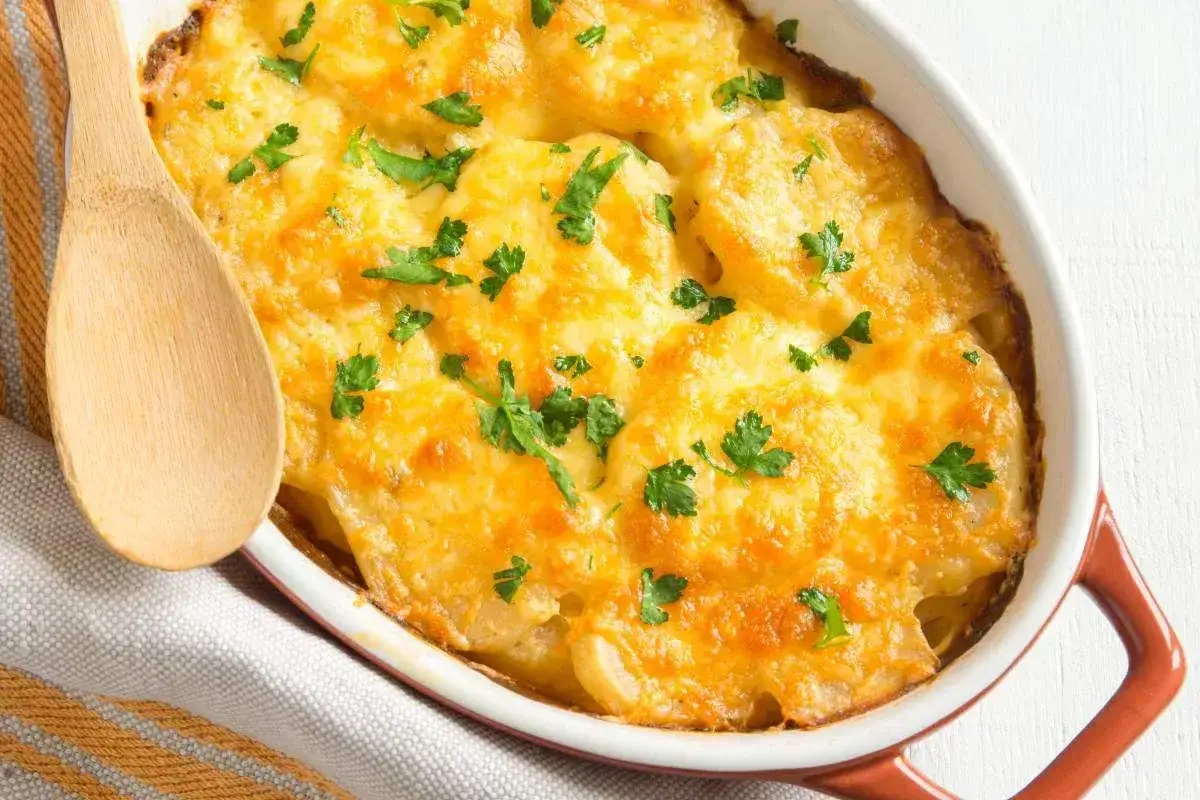 Un gratin de l&eacute;gumes dor&eacute; et gratin&eacute;, garni de persil frais. Une cuill&egrave;re en bois est pos&eacute;e sur le bord du plat.