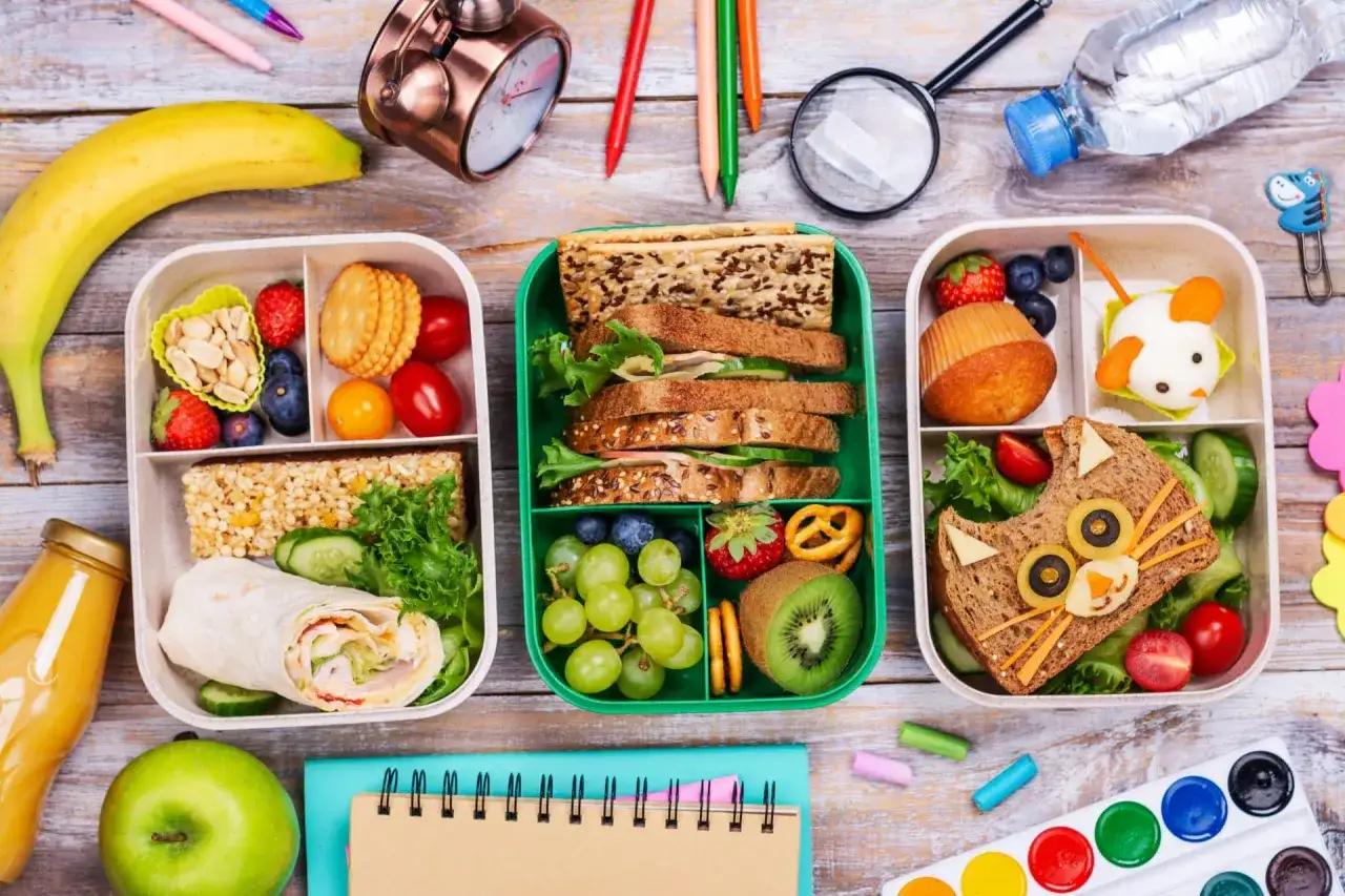 Un pique-nique ado prêt pour l'école : sandwichs créatifs, fruits, et gourmandises dans des boîtes colorées.