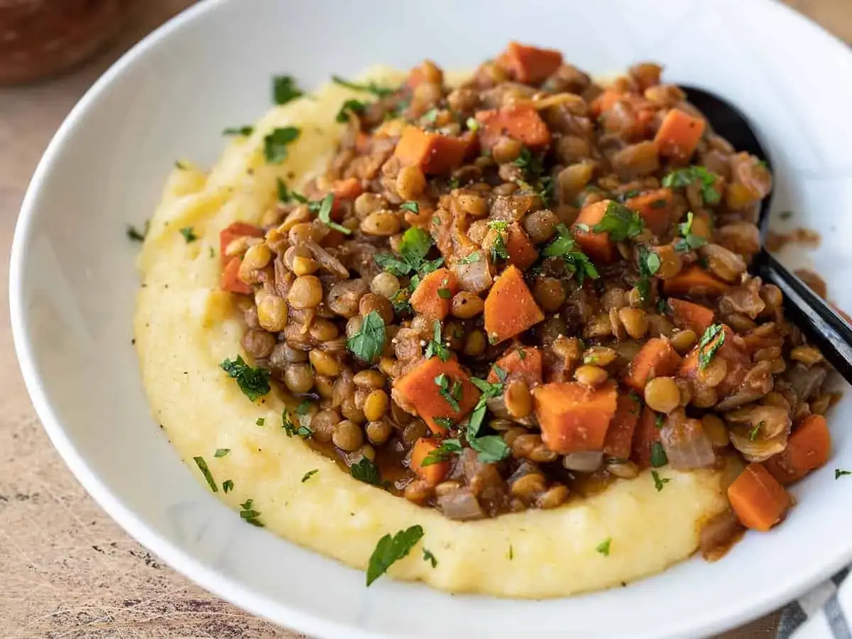 Un plat r&eacute;confortant de lentilles et carottes sur une pur&eacute;e de polenta cr&eacute;meuse. Une recette pas cher et saine, garnie de persil frais.