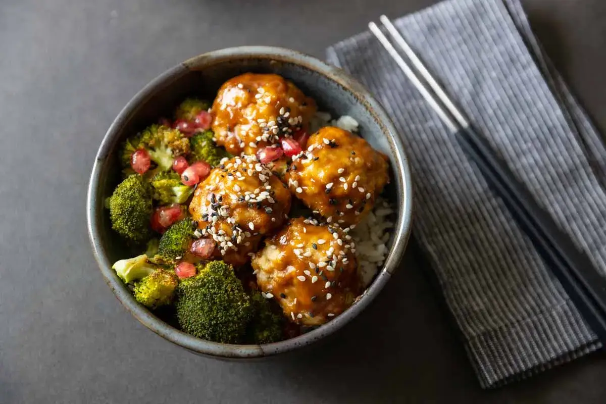 Un bol appétissant de recette boulette de poulet asiatique, garni de brocolis, de graines de sésame et de grenade.