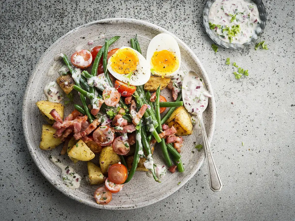 Salade gourmande avec haricots verts, pommes de terre r&ocirc;ties, tomates cerises, lardons croustillants et &oelig;uf mollet, napp&eacute;e d'une sauce cr&eacute;meuse.