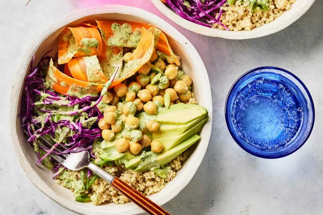 Un plat v&eacute;g&eacute;tarien color&eacute; avec du quinoa, des pois chiches, de l'avocat, des carottes et du chou rouge, arros&eacute; d'une sauce verte cr&eacute;meuse.