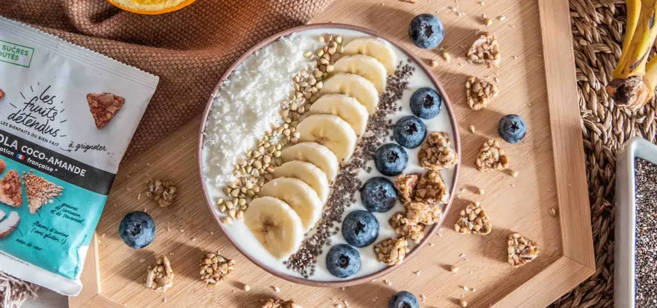 Un bol de smoothie aux fruits avec bananes, myrtilles, noix de coco râpée, graines de chia et de sarrasin. Parfait pour savoir quoi manger le midi !