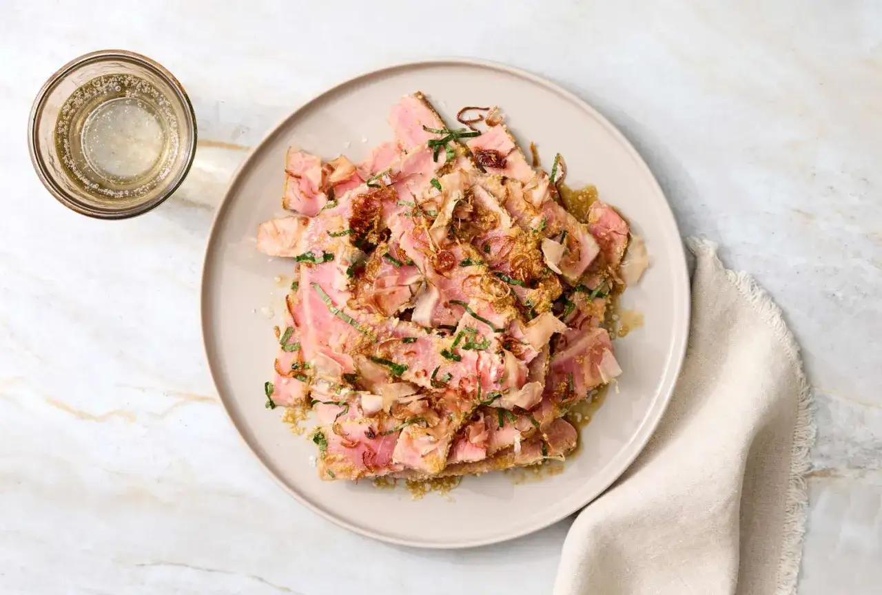Tataki de thon, un plat savoureux avec un accompagnement de fines herbes et d'oignons frits, servi avec un verre de boisson pétillante.