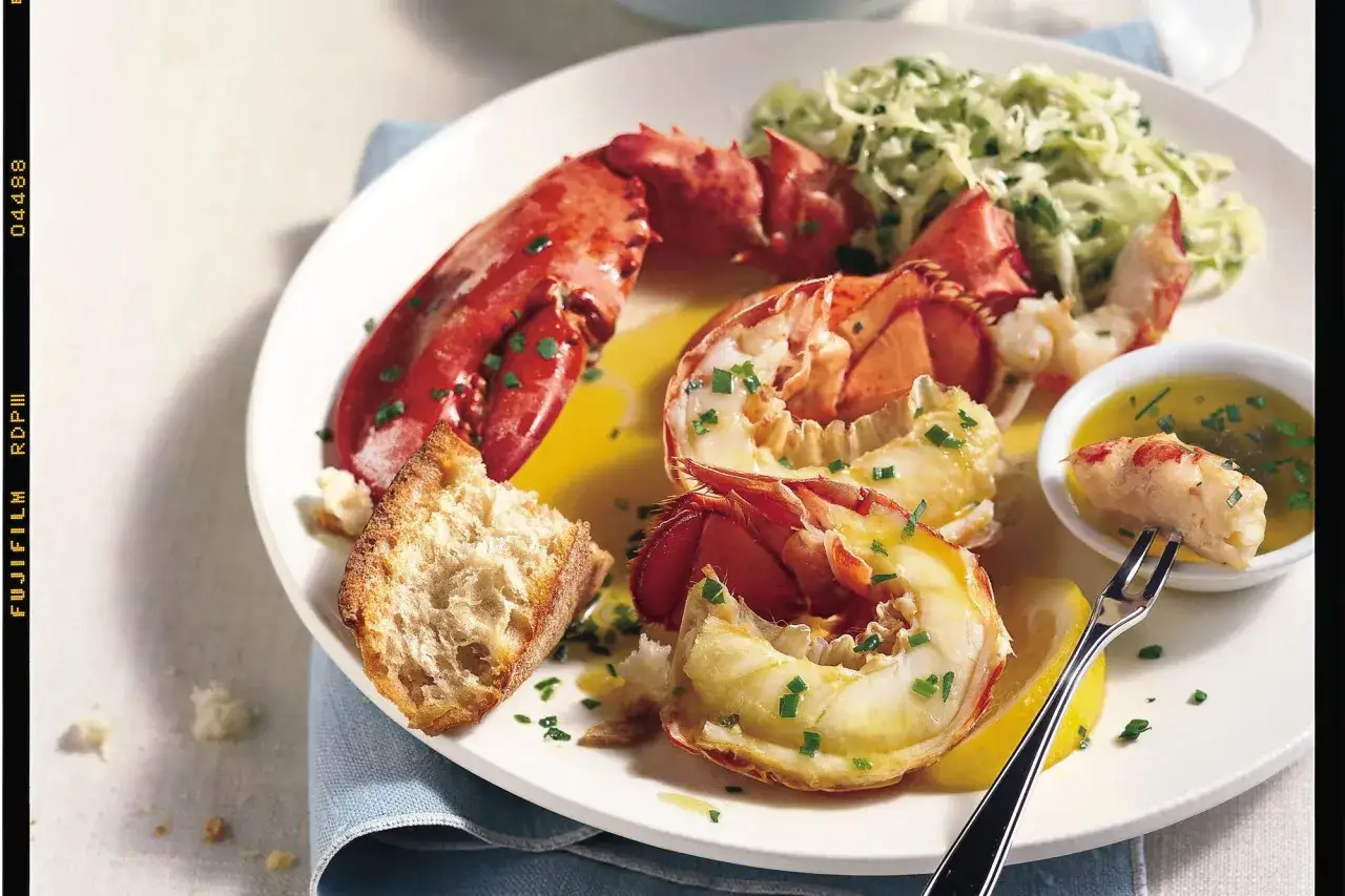 Homard cuit, servi avec du pain croustillant, une salade fraîche et une sauce au beurre. La cuisson du homard est parfaite, la chair est tendre et savoureuse.