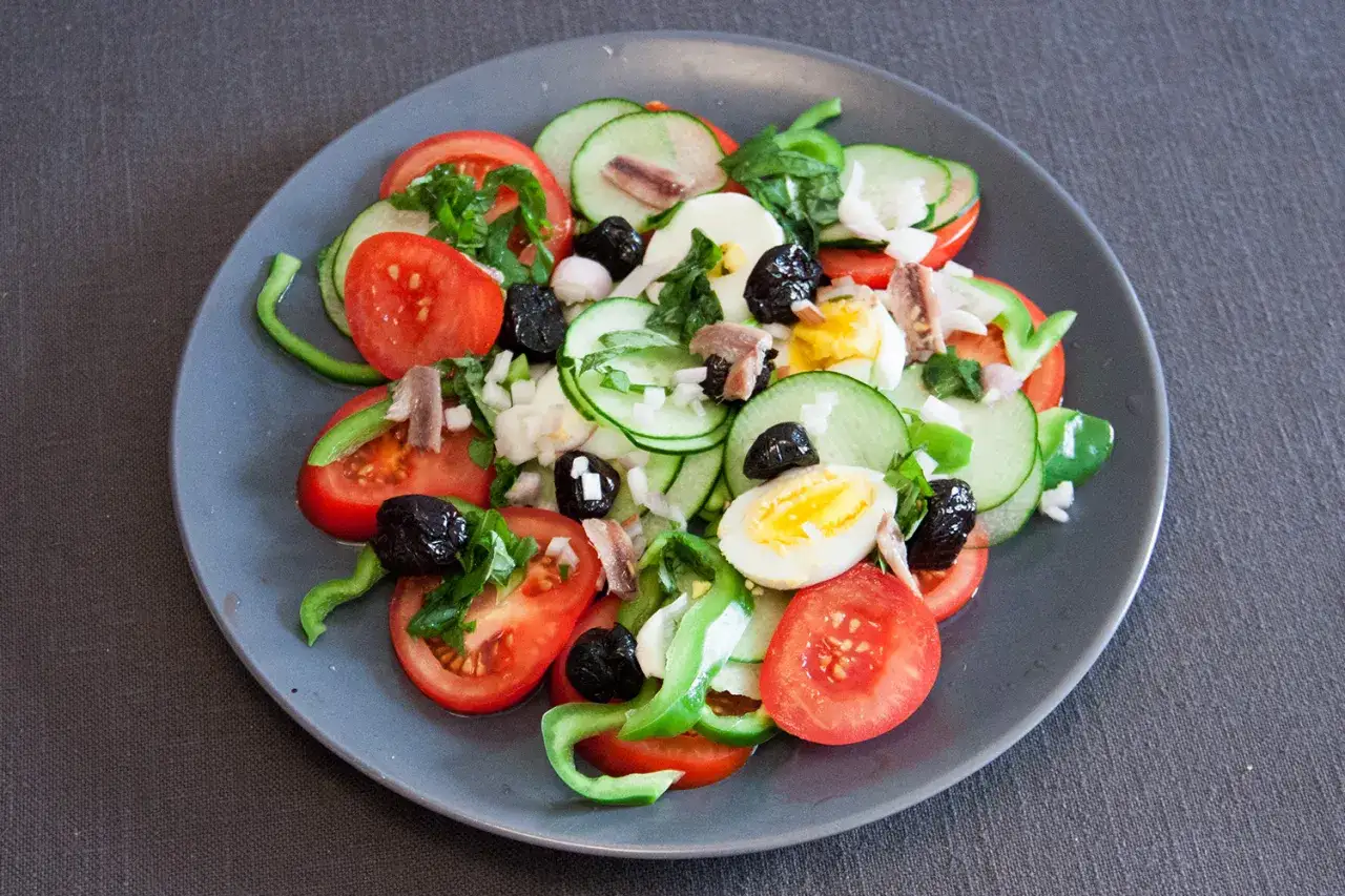 Salade ni&ccedil;oise color&eacute;e avec tomates, concombres, &oelig;ufs durs, olives noires et anchois.