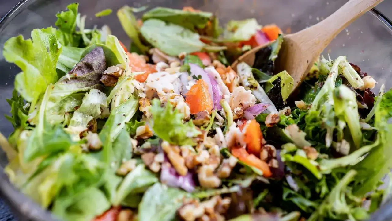Salade de légumes verts frais avec noix, oignons rouges et morceaux de poulet. Une cuillère en bois mélange cette salade colorée.