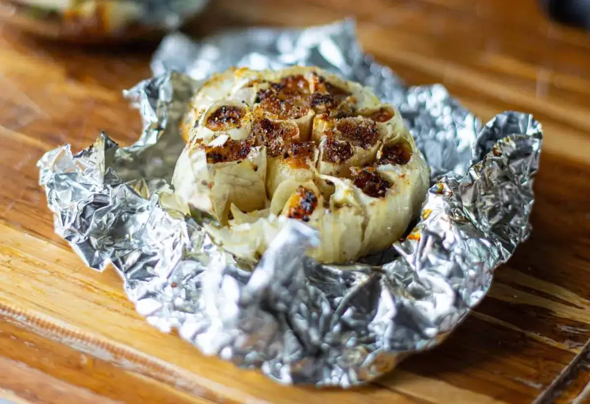 Ail en papillote, dor&eacute; et fondant, pr&ecirc;t &agrave; &ecirc;tre d&eacute;gust&eacute; sur un fond en bois.