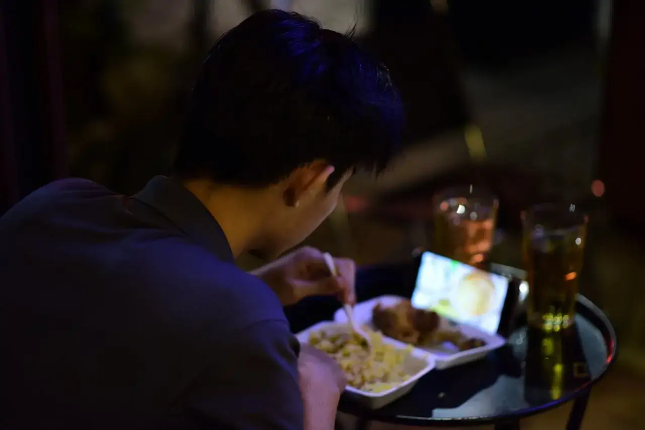 Un homme mange son panier repas travail de nuit, devant son t&eacute;l&eacute;phone.