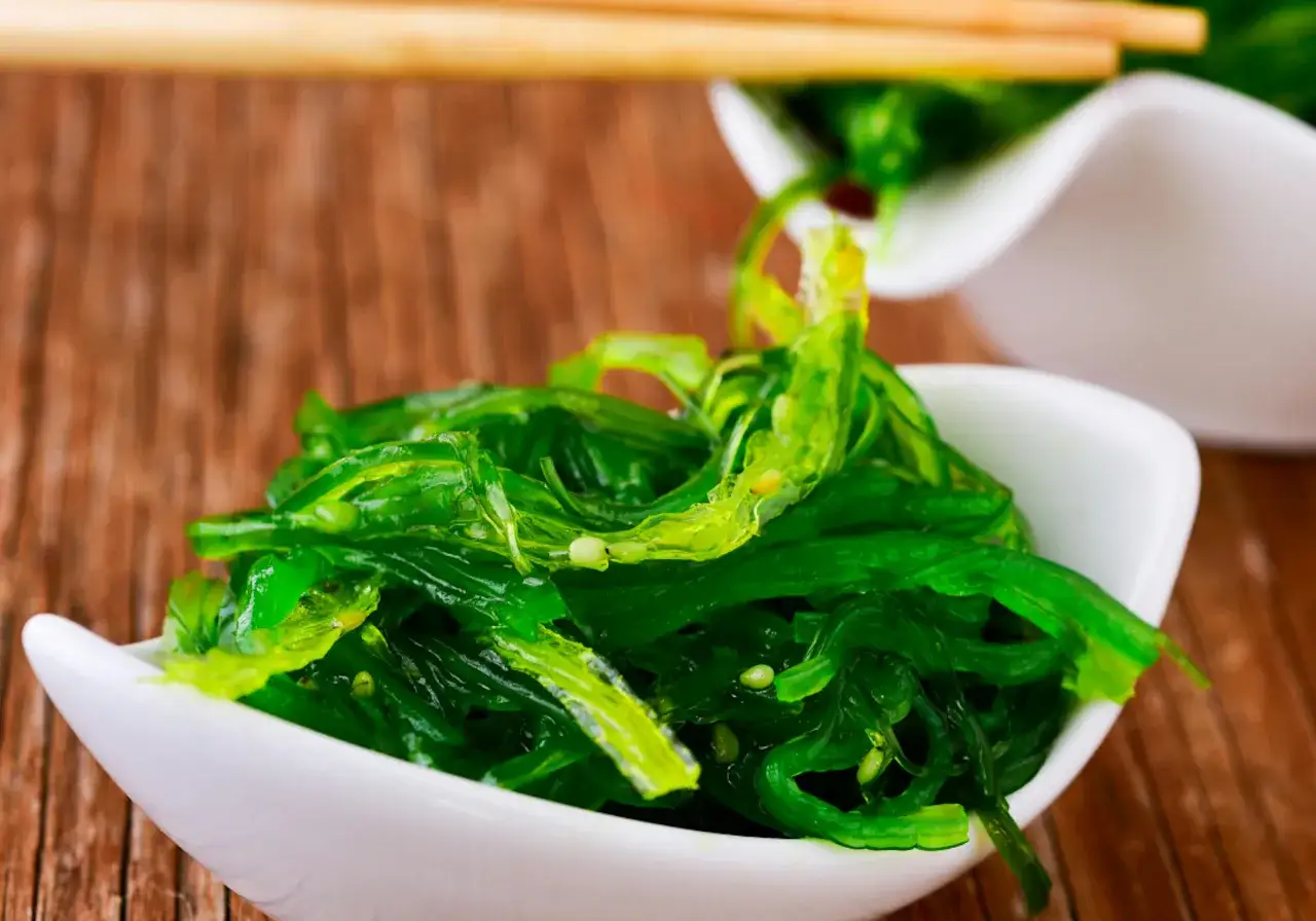 Salade d'algue japonaise fra&icirc;che, servie dans un bol blanc sur fond de bois.