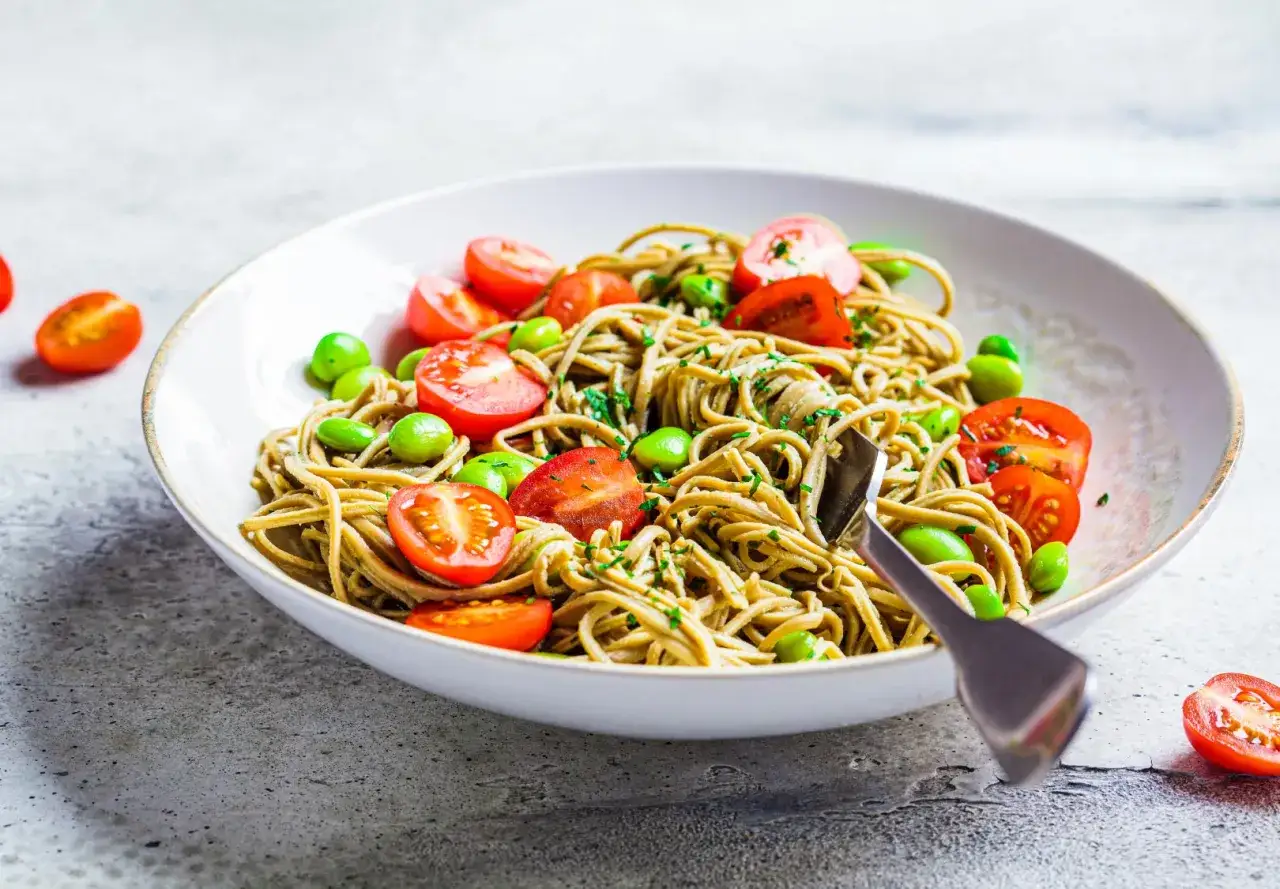 Un plat de pâtes aux edamames, tomates cerises et persil, servi dans un bol blanc.