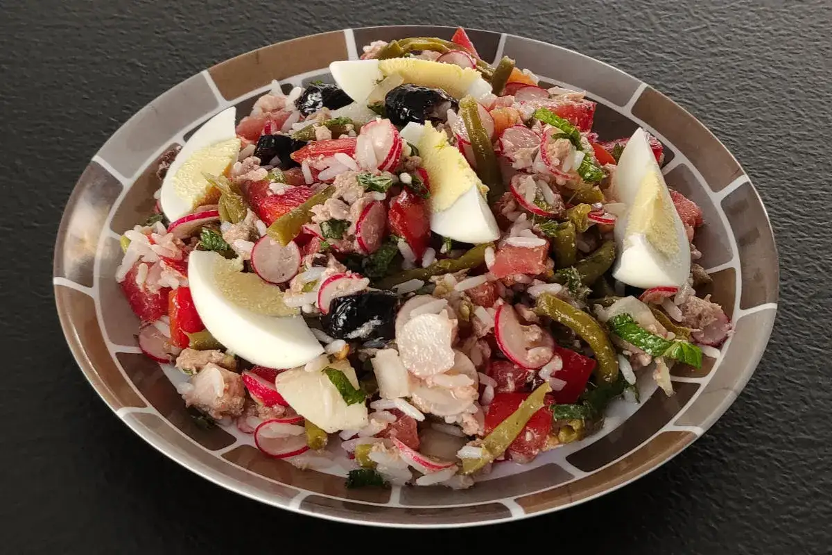 Une salade ni&ccedil;oise riz g&eacute;n&eacute;reuse avec thon, &oelig;ufs, haricots verts, tomates, radis et olives noires sur une assiette d&eacute;cor&eacute;e.