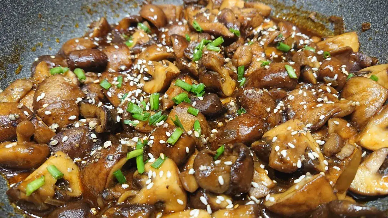Champignons caramélisés chinois, brillants et appétissants, parsemés de graines de sésame et de ciboule fraîche.