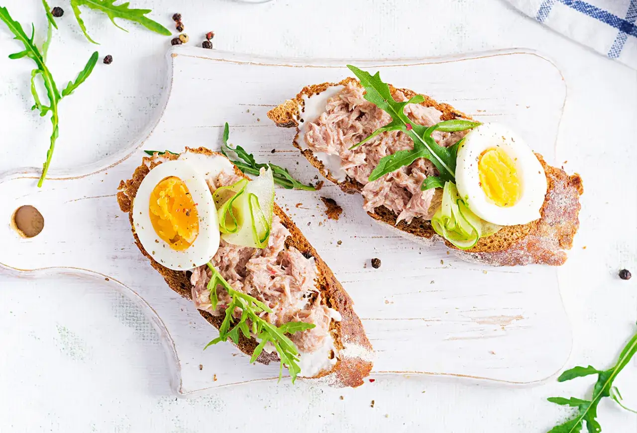 Deux tartines de pain noir garnies de rillettes de thon, d'&oelig;uf dur, de concombre et de roquette.