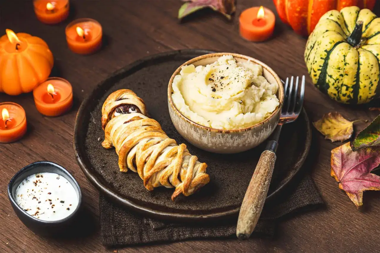 Un menu d'Halloween pour adultes : une momie feuillet&eacute;e avec pur&eacute;e de pommes de terre, entour&eacute;e de bougies et de citrouilles.