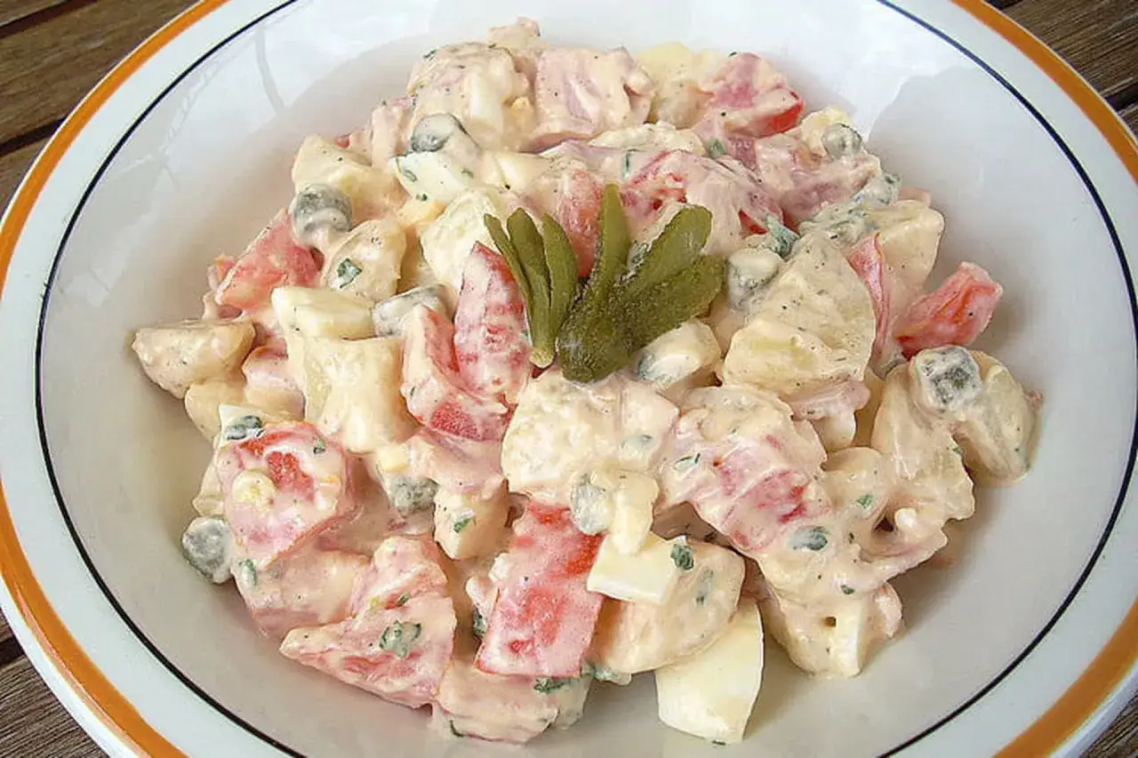 Salade piémontaise crémeuse avec pommes de terre, tomates, œufs et cornichons, garnie d'une feuille de persil.