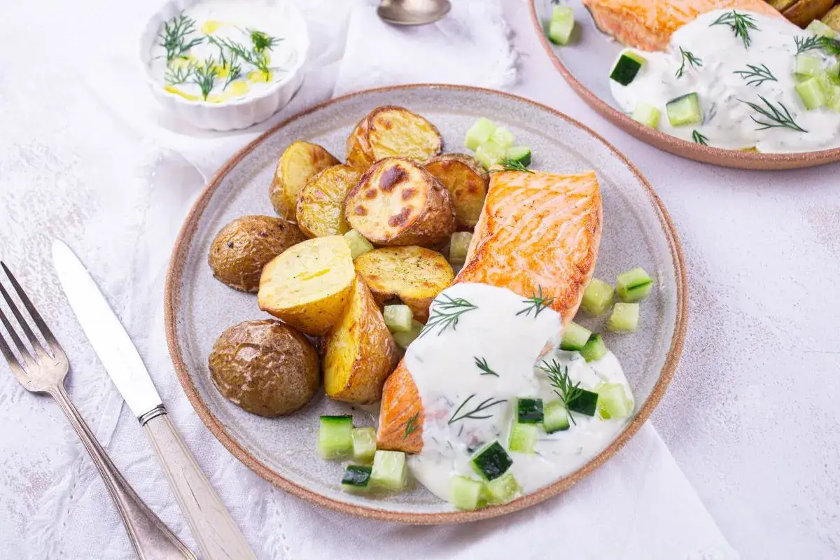Un filet de saumon grillé, pommes de terre rôties et sauce au yogourt et concombre, parfait pour une recette salade nordique.