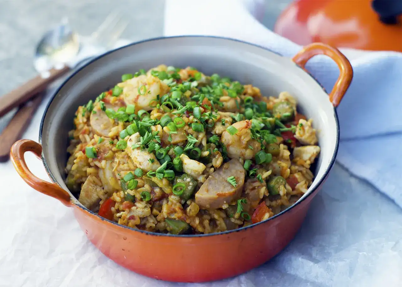 Un plat de jambalaya coloré, garni de crevettes, poulet, saucisse et oignons verts, prêt à être dégusté.