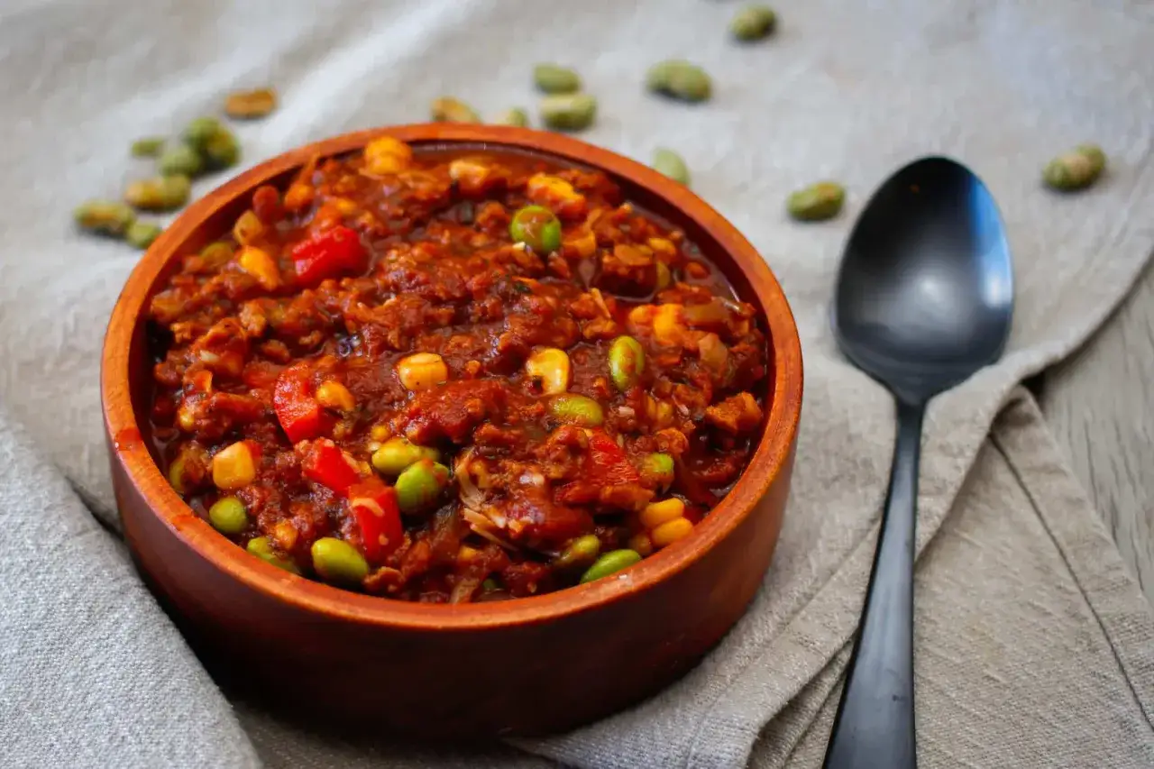 Un bol de chili v&eacute;g&eacute;tarien savoureux, garni de ma&iuml;s et de haricots edamame, pr&ecirc;t &agrave; &ecirc;tre d&eacute;gust&eacute; avec une cuill&egrave;re.