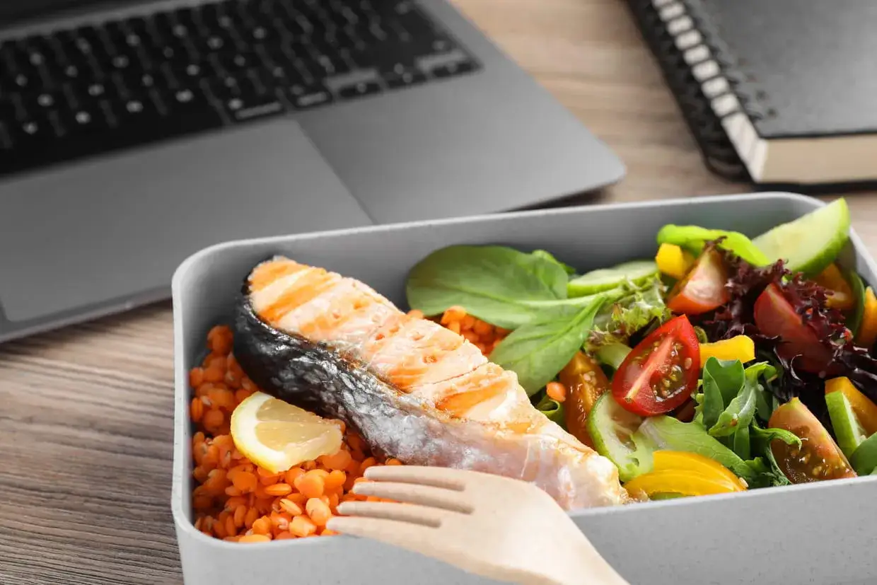 Un plat à emporter fait maison avec saumon grillé, lentilles corail et salade fraîche. Parfait pour un déjeuner sain au bureau.