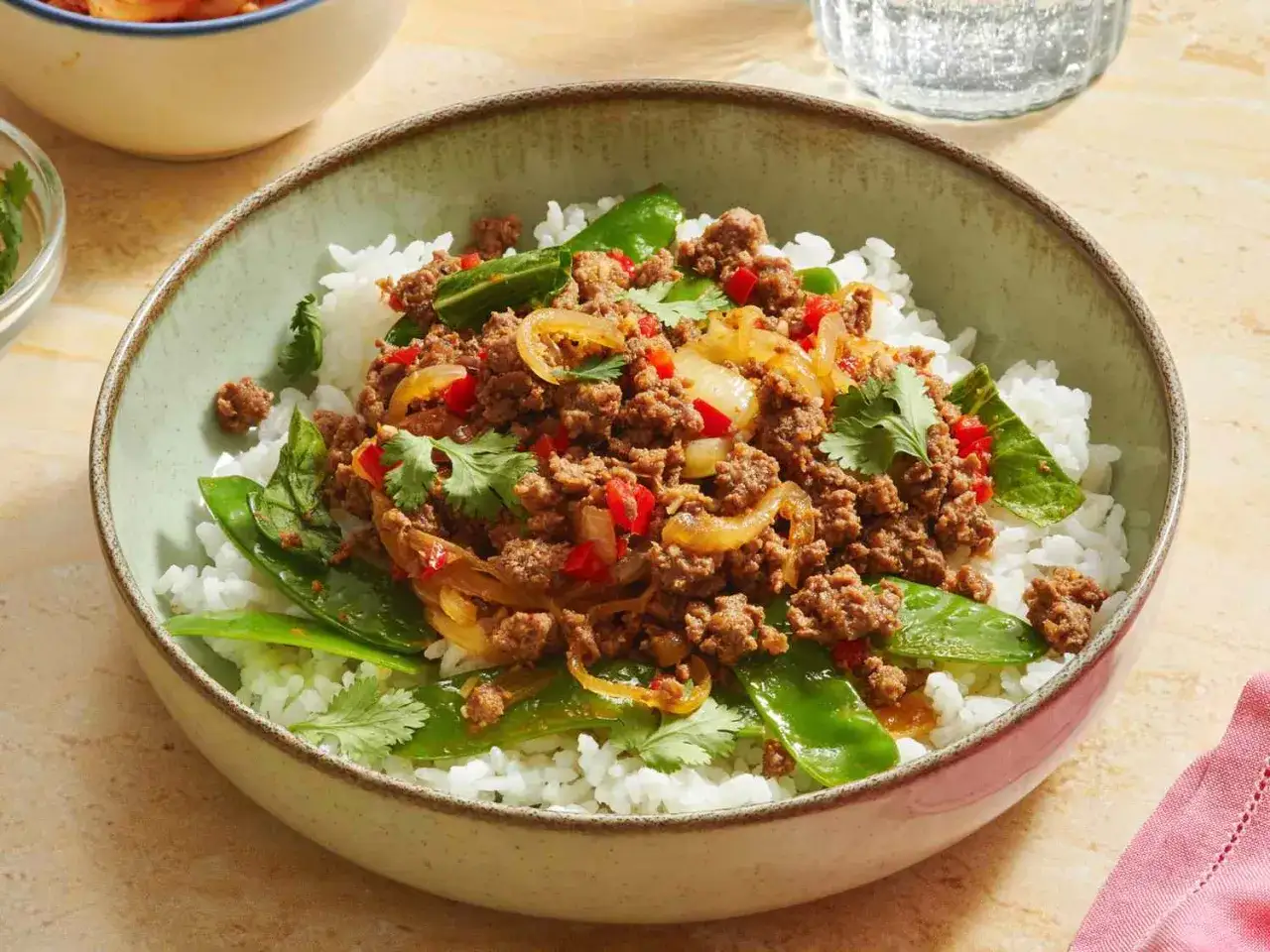Un délicieux sauté boeuf haché asiatique sur un lit de riz blanc, garni de pois gourmands et de coriandre fraîche.