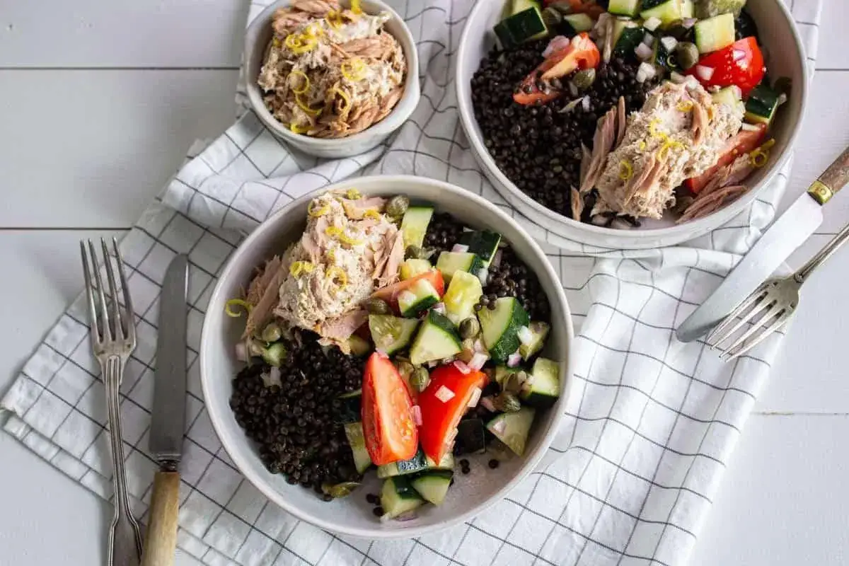 Deux bols de salade de thon avec lentilles, concombre, tomate et câpres, garnie de zeste de citron.