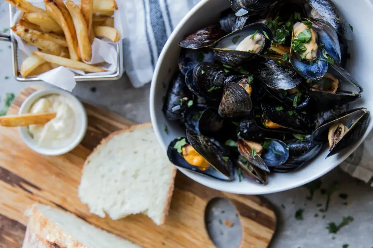 Un plat de moules au ros&eacute;, servi avec des frites croustillantes, du pain frais et une sauce cr&eacute;meuse. Un d&eacute;lice pour les amateurs de fruits de mer.