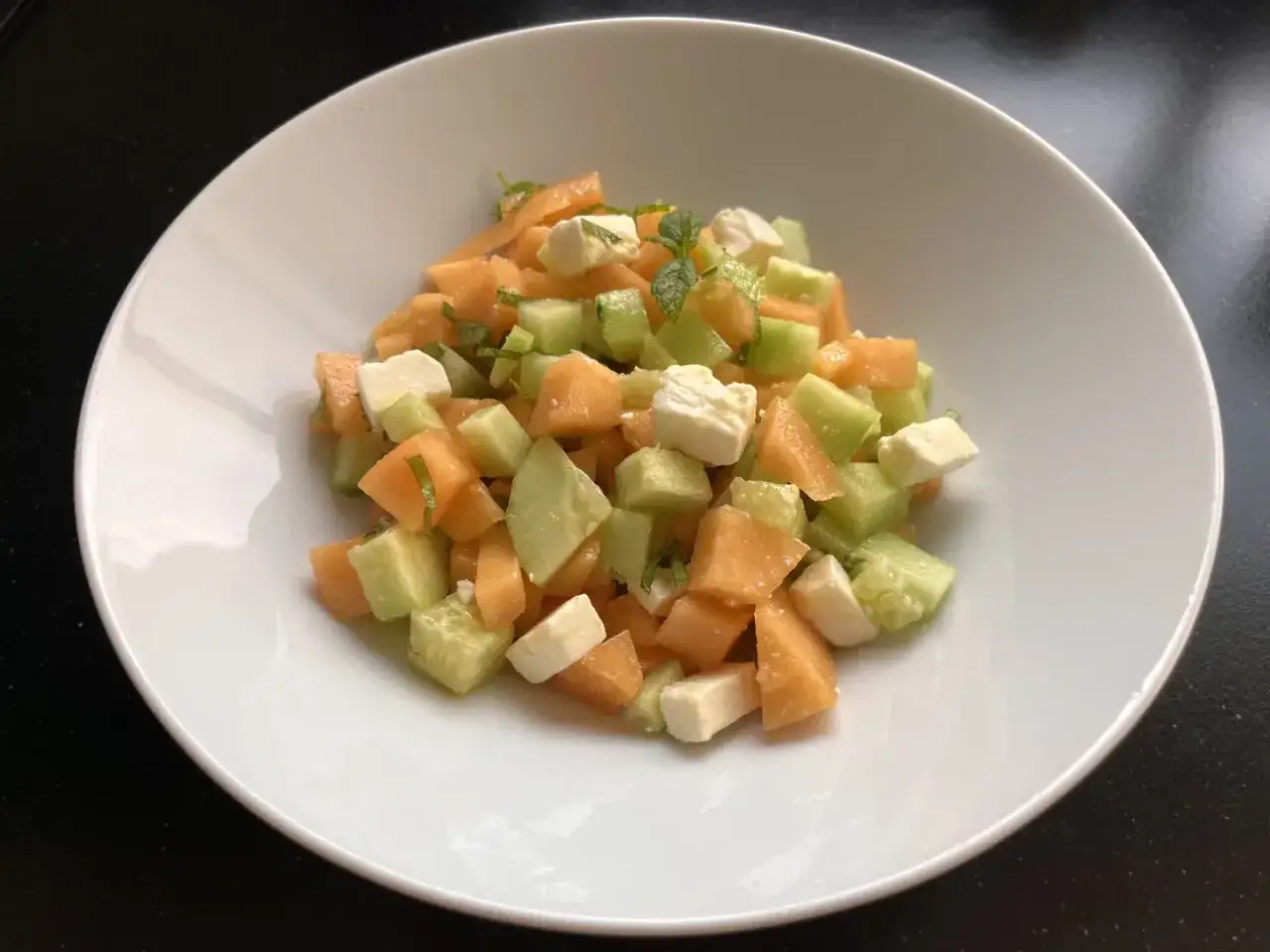Salade melon feta fraîche et colorée, avec des dés de concombre et des feuilles de menthe.