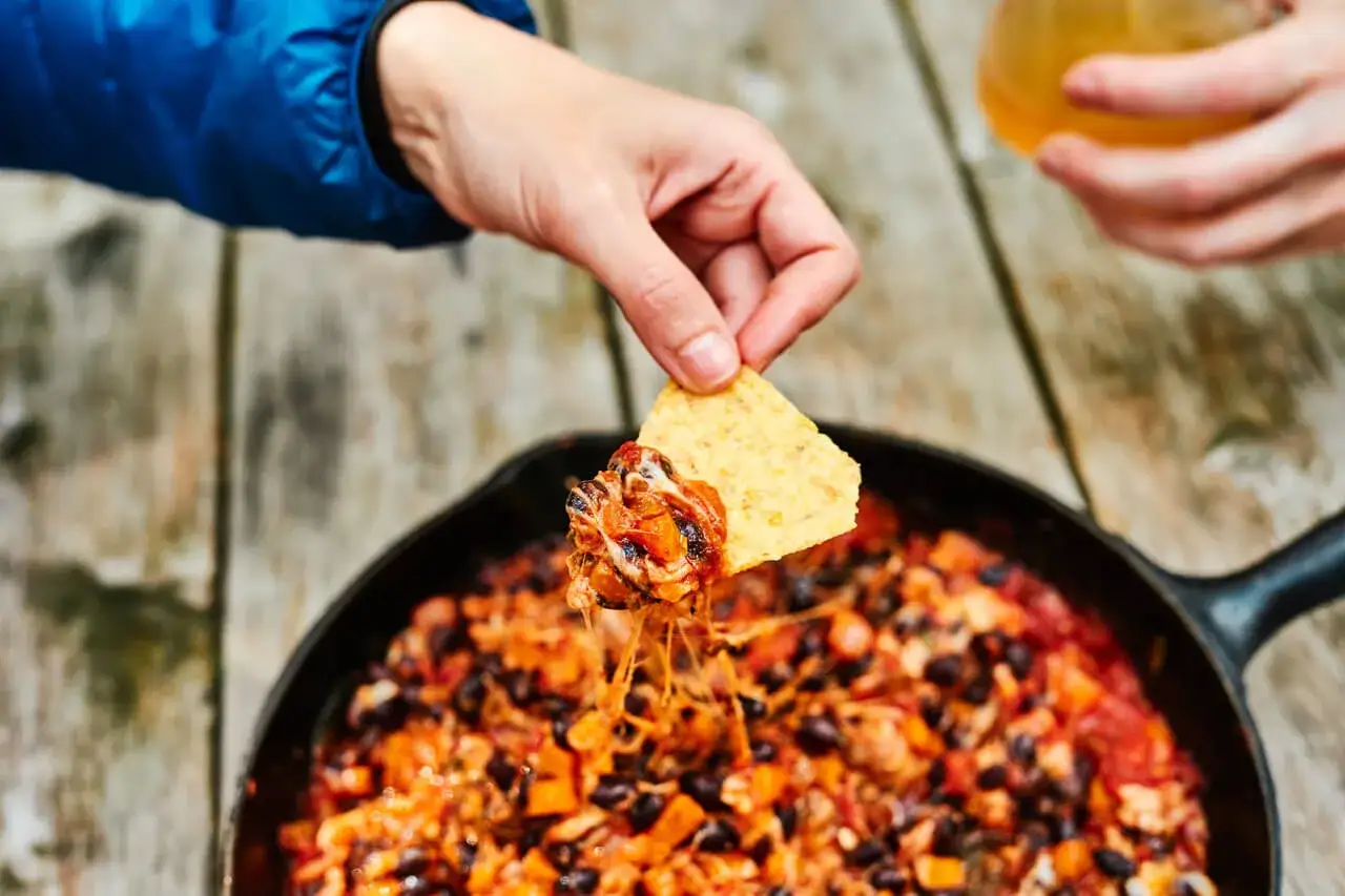Une id&eacute;e repas camping : une po&ecirc;le de chili aux haricots noirs et fromage fondant, tremp&eacute;e avec une tortilla.
