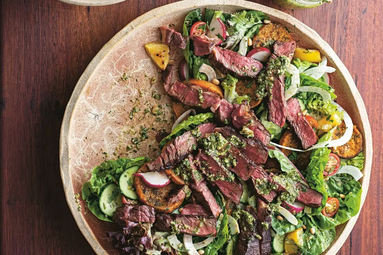 Une généreuse salade kobe, garnie de fines tranches de bœuf grillé, de légumes frais et d'une sauce verte vibrante, le tout servi sur une assiette rustique.