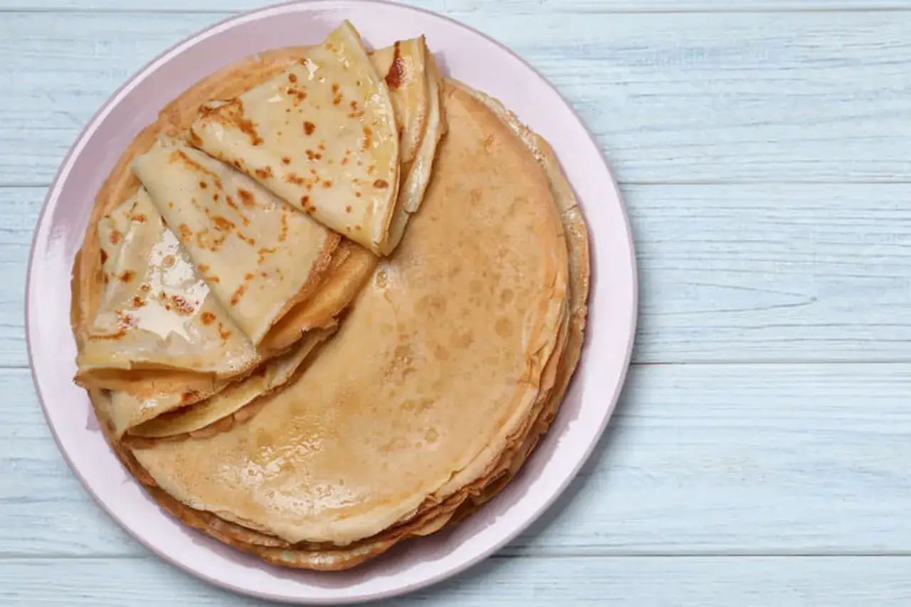 Pile de cr&ecirc;pes dor&eacute;es sur une assiette rose. Ces d&eacute;licieuses cr&ecirc;pes vegan sont pr&ecirc;tes &agrave; &ecirc;tre garnies.