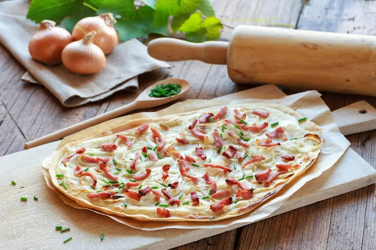 Tarte flambée garnie d'oignons et de lardons, avec une touche d'ail confit.