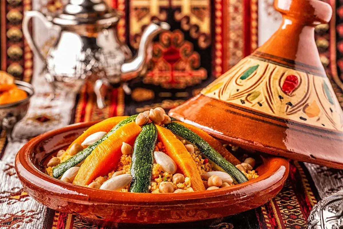 Un plat de couscous marocain color&eacute; avec des l&eacute;gumes, des pois chiches et des amandes, servi dans un plat en terre cuite traditionnel.