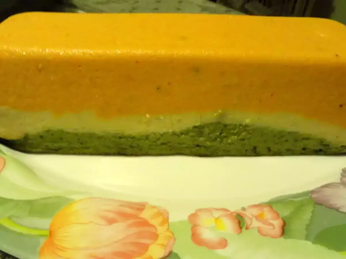 Une terrine de légumes aux trois couleurs : orange, blanc et vert. Elle repose sur une assiette décorée de tulipes.