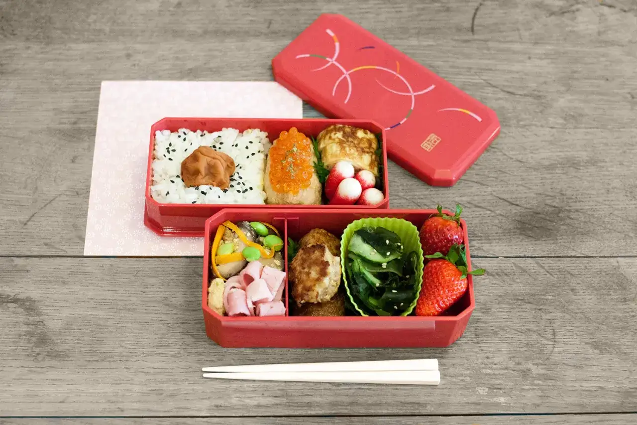 Délicieux repas japonais maison : riz, saumon, tamagoyaki, légumes, viande et fraises dans une boîte bento rouge.