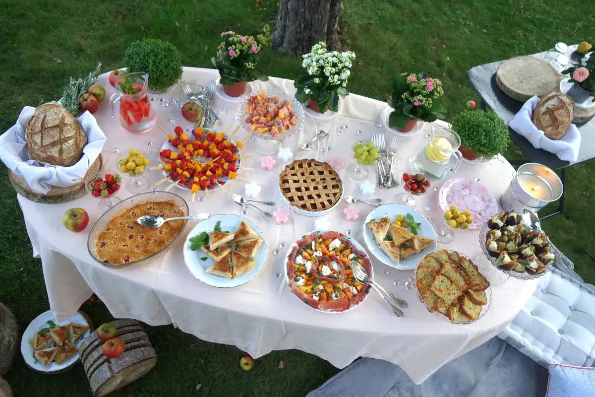 Un magnifique buffet pour une id&eacute;e pique-nique : tartes, brochettes de fruits, salades, pain et desserts, le tout dress&eacute; sur une table en ext&eacute;rieur.