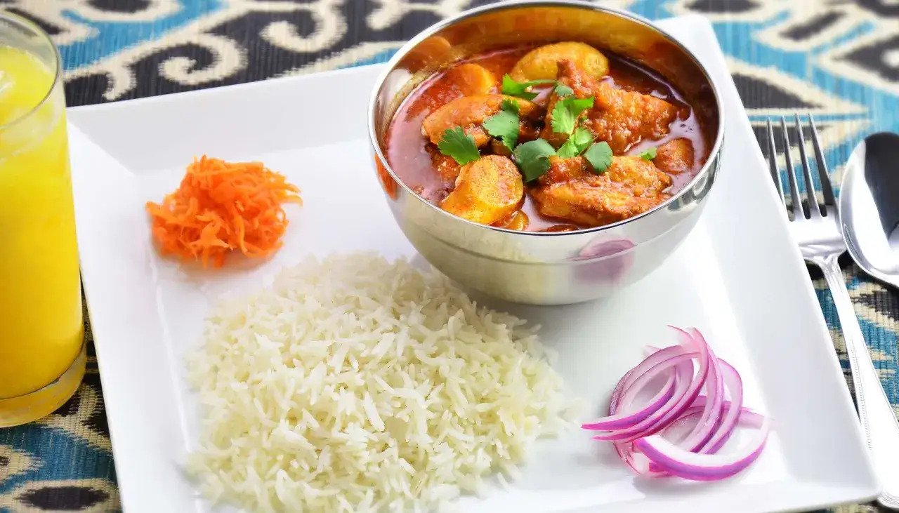 Un plat de poulet vindaloo, c'est quoi ? Un curry &eacute;pic&eacute; avec du riz, des carottes r&acirc;p&eacute;es, des oignons rouges et une boisson jaune.