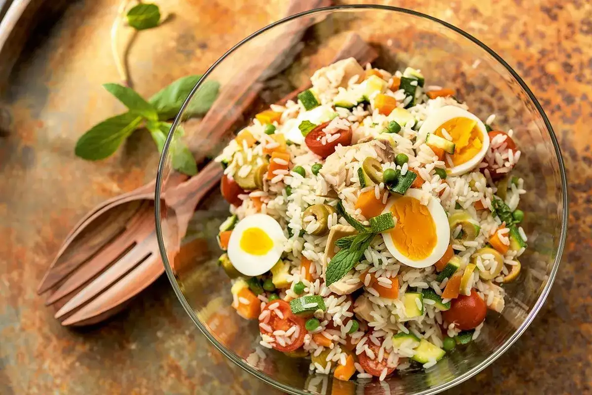 Salade de riz thon colorée avec œufs durs, tomates, olives, petits pois et courgettes. Un plat frais et complet.