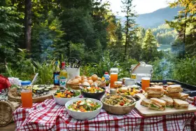 Un festin en plein air : salades, sandwichs, fruits et boissons sur une table de pique-nique. Une belle idée repas camping pour profiter de la nature.