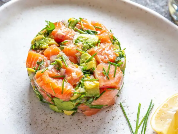 Un délicieux tartare saumon avocat, frais et coloré, garni de ciboulette et servi avec un quartier de citron.