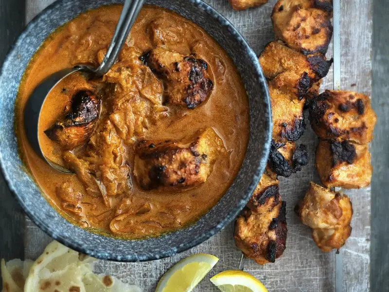 Un plat de poulet tikka savoureux, avec des morceaux de poulet grillés dans une sauce crémeuse et des accompagnements comme du pain naan et des quartiers de citron.