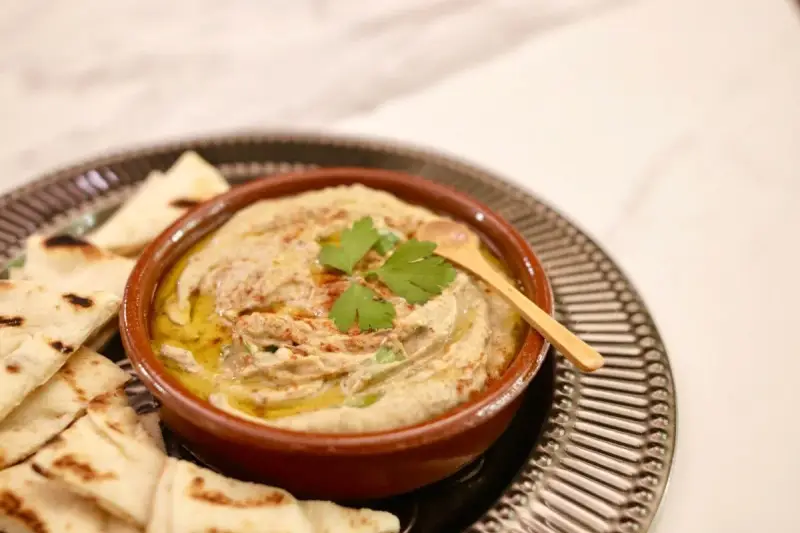 Un bol de baba ganoush crémeux, garni de persil frais et d'un filet d'huile d'olive, servi avec des pains pita grillés.